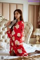 A woman in a red kimono sitting on a bed holding a fan.