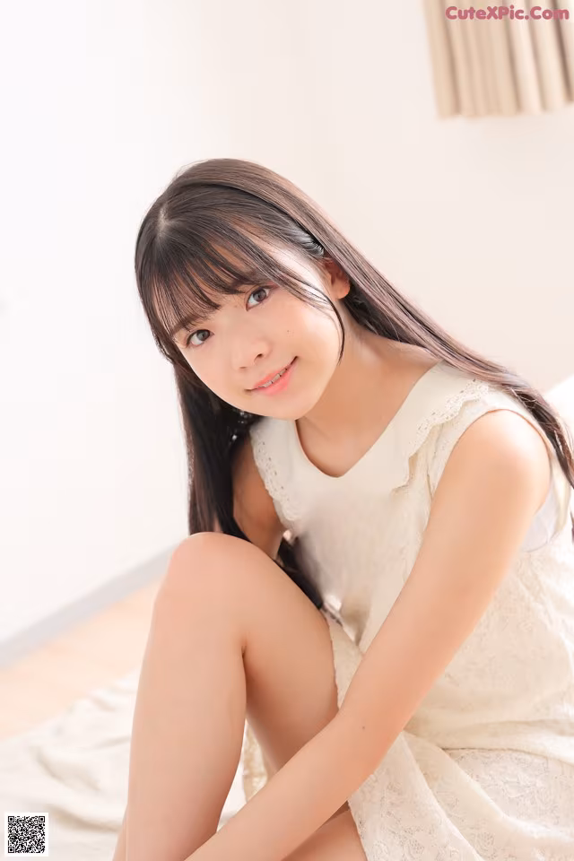 A woman in a white dress sitting on a bed.
