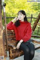 A woman sitting on a wooden bench wearing a red sweater.