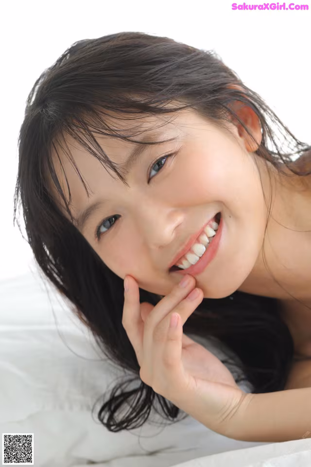 A young woman laying on a bed with her hand on her chin.