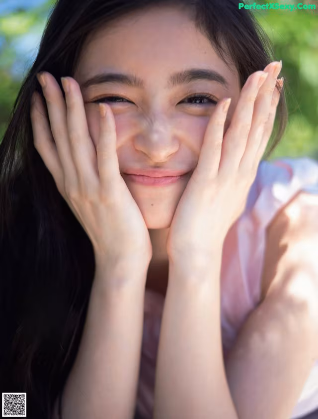 A woman with long black hair covering her face with her hands.
