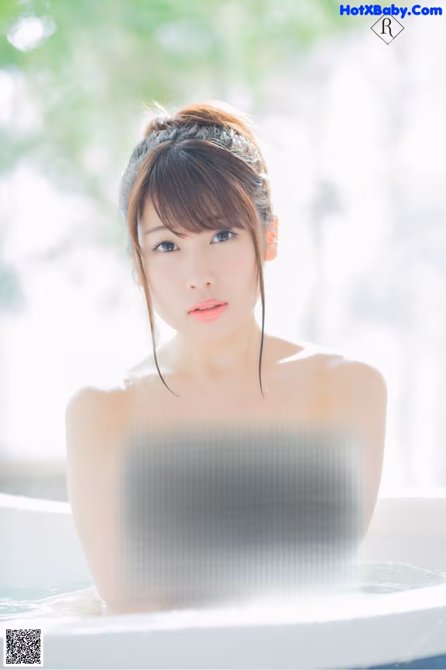 A naked woman sitting in a bathtub with water on her breasts.