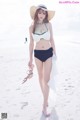 A woman in a bikini and hat walking on the beach.