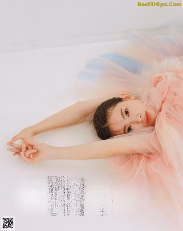 A woman in a pink tutu laying on a white surface.