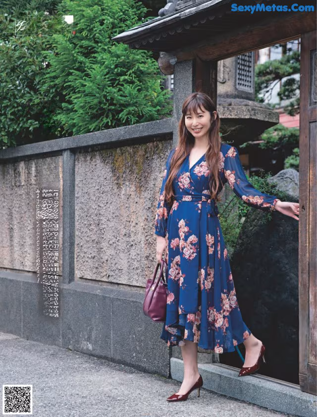 A woman in a blue floral dress standing in front of a building.