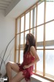 A woman in a red lingerie sitting on a window sill.