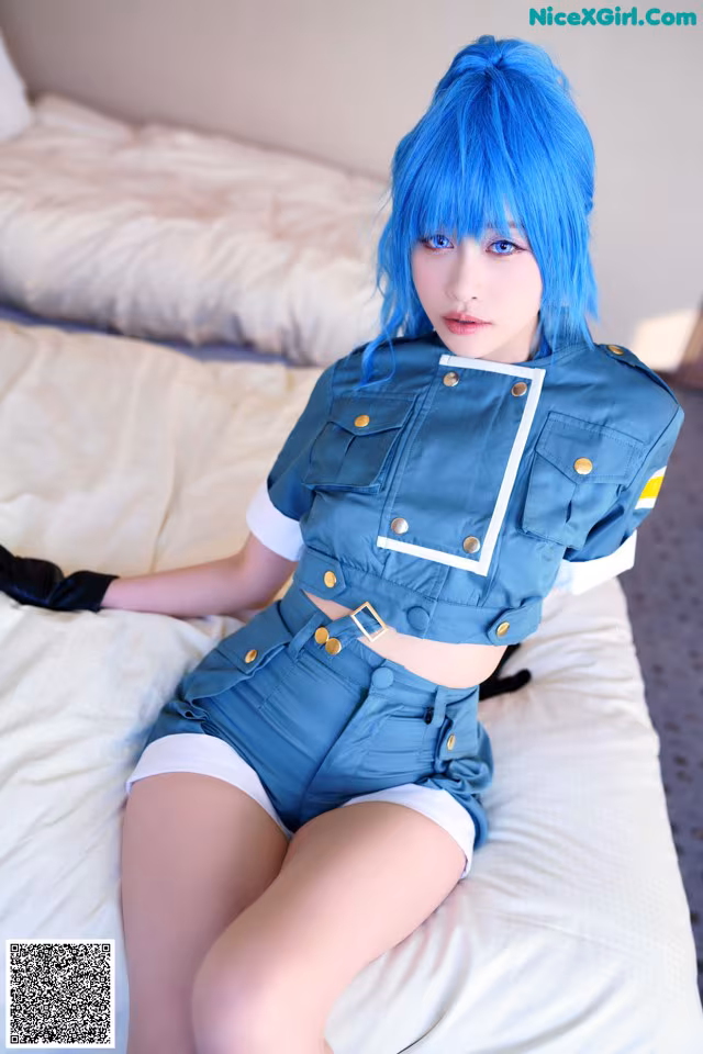 A woman with blue hair sitting on a bed.