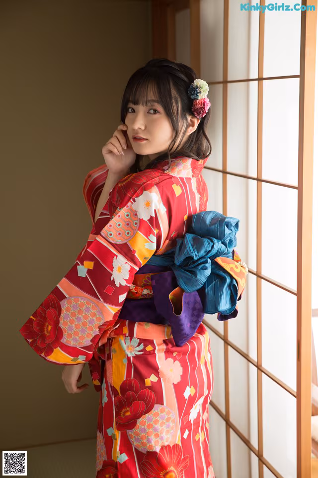 A woman in a red kimono standing in front of a window.
