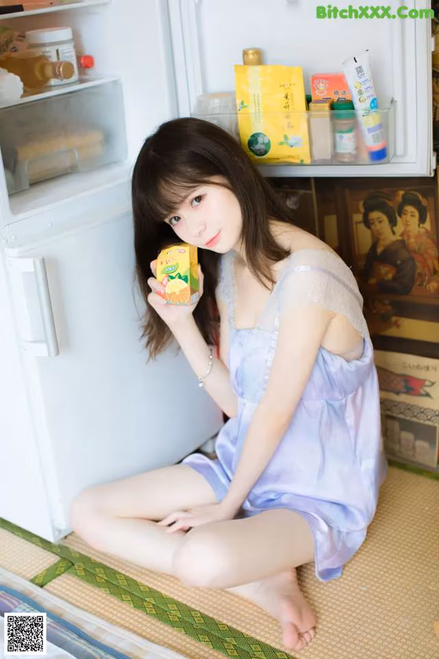 A woman sitting on the floor holding a box of orange juice.