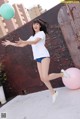 A woman in a white shirt and blue shorts jumping in the air.