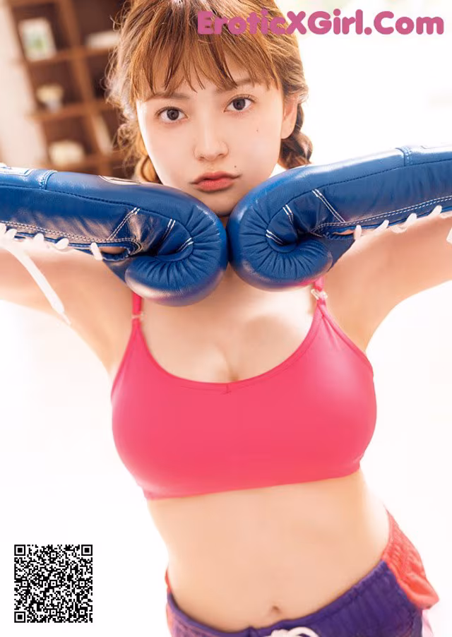 A woman in a pink top and blue boxing gloves.