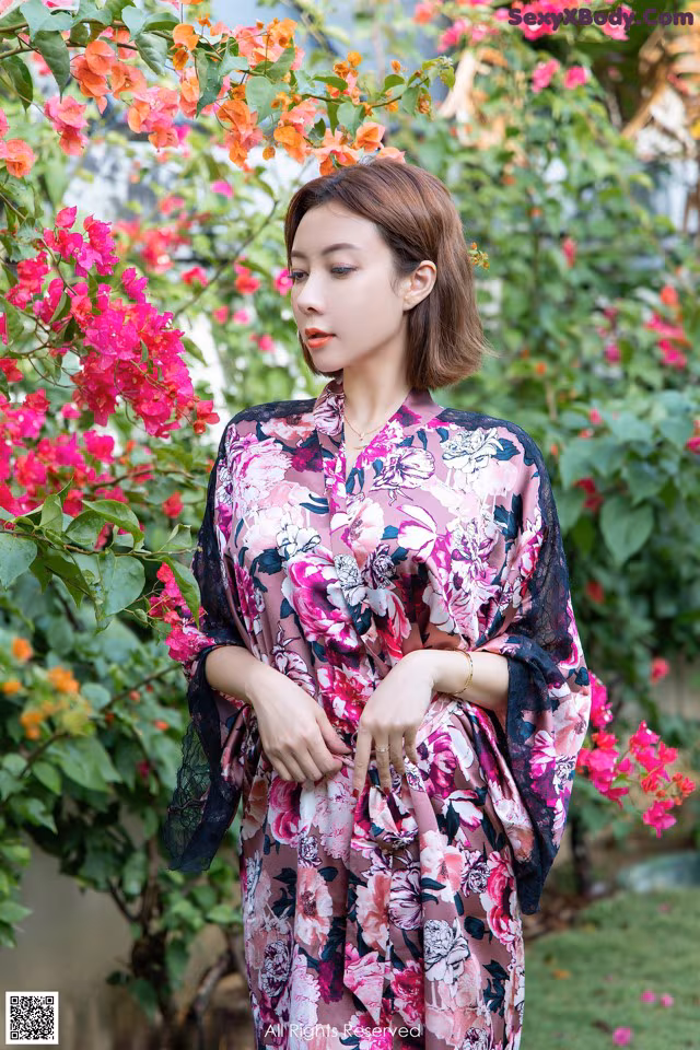 A woman standing in front of a bush of flowers.