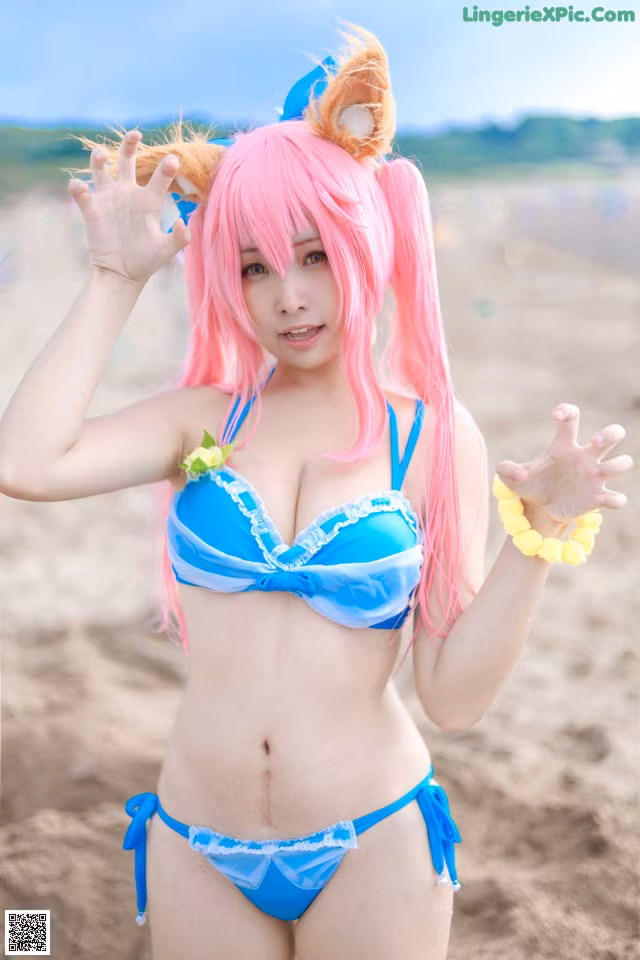 A woman in a blue bikini with pink hair on the beach.
