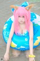 A woman with pink hair sitting on an inflatable ring in the water.