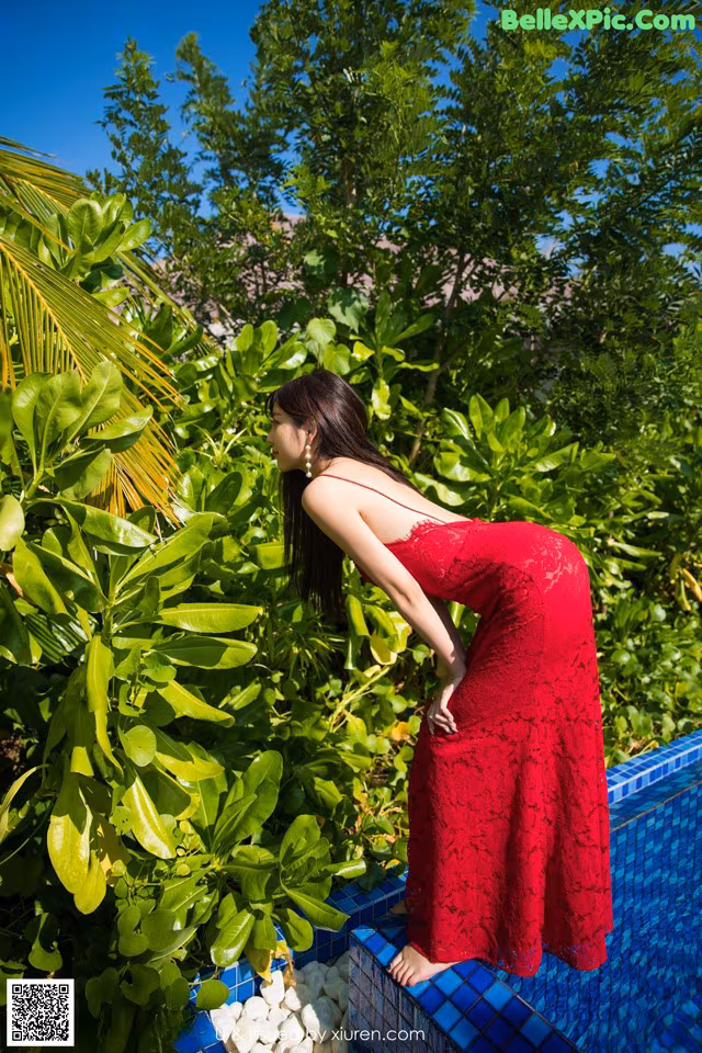 A woman in a red dress standing next to a swimming pool.