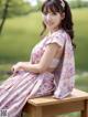 A woman in a pink dress sitting on a wooden bench.