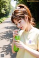 A woman in a yellow shirt drinking from a green bottle.