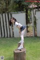 A young woman in a school uniform is posing on a tree stump.